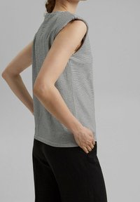 Pruhovaná bezramenná halenka v černé a bílé barvě s volným střihem. Má kulatý výstřih a jemnou, lehkou látku. Jednoduchý design, bez vzorů.