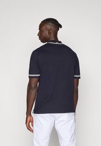 Polo de cor azul marinho feito de algodão, com colarinho clássico, mangas curtas com riscas brancas e um corte descontraído.