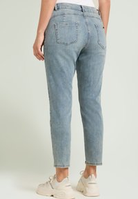 Vaqueros de tiro alto de color azul claro, con corte recto, bolsillos traseros y una sutil textura desvaída. Combinados con zapatillas de color crema.