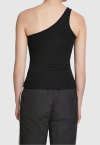 Haut sans manches noir, ajusté, avec une seule bretelle, en coton lisse, présentant un design contemporain. Porté avec un pantalon noir texturé.
