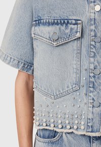 Lichtblauwe denim cropped jack met korte mouwen, voorzien van een voorzak, zilveren hardware en versieringen van parels en strass.