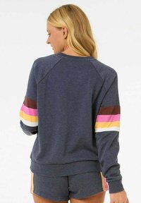 Donkerblauwe sweatshirt met kleurrijke gestreepte accenten in roze, geel en bruin op de mouwen. De stof lijkt zacht met een relaxte pasvorm.