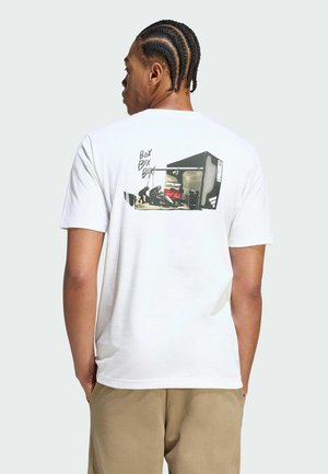 Young man with cornrow hairstyle wearing a white t-shirt featuring a garage scene with a car and "BOX BOX BOX" text on the back.