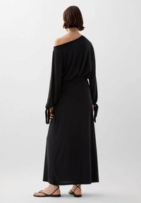 Abito maxi nero off-the-shoulder realizzato in tessuto morbido, con maniche lunghe con chiusure a cravatta e una vestibilità rilassata fino alle caviglie.