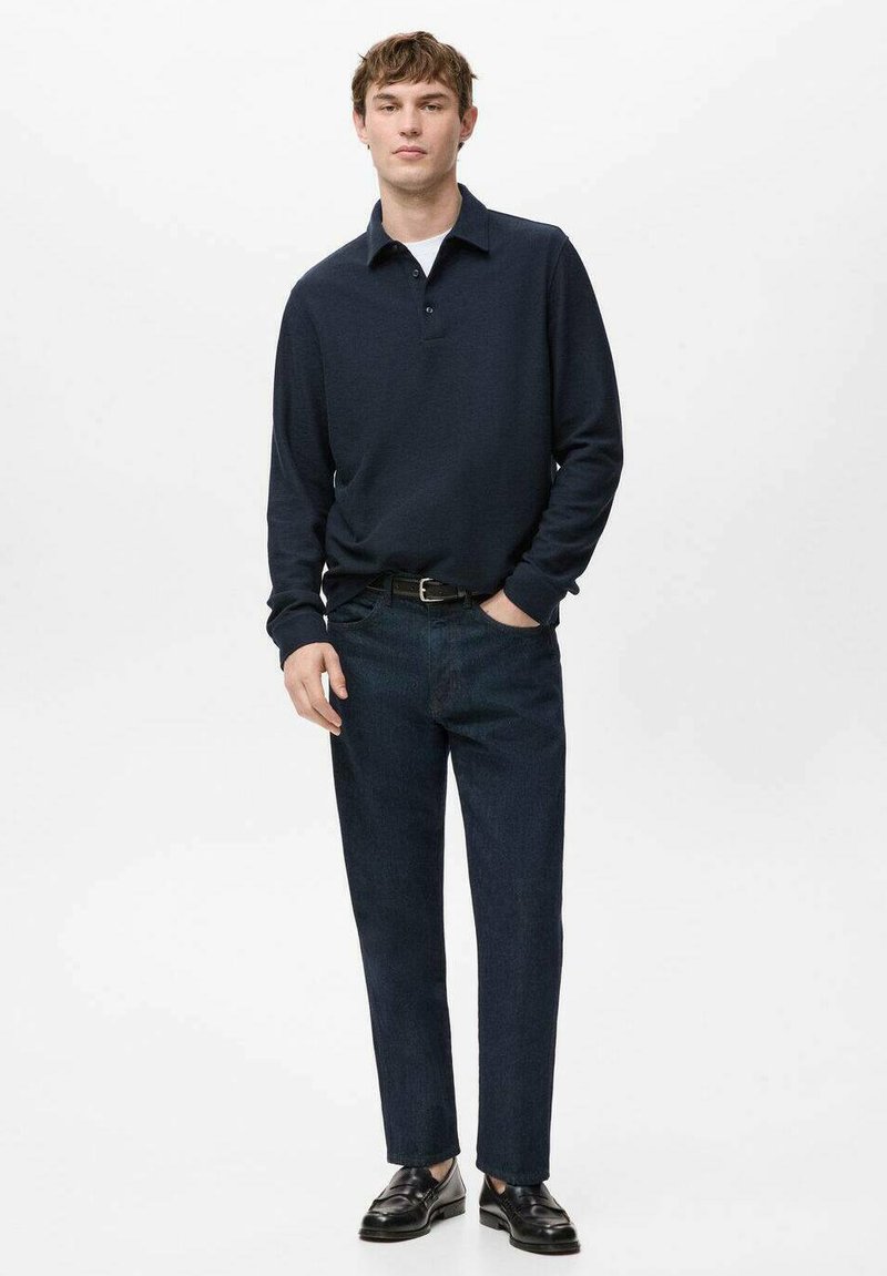 Polo à manches longues bleu marine avec col, associé à un pantalon en denim foncé et des chaussures noires. Tissu lisse et coupe ajustée.