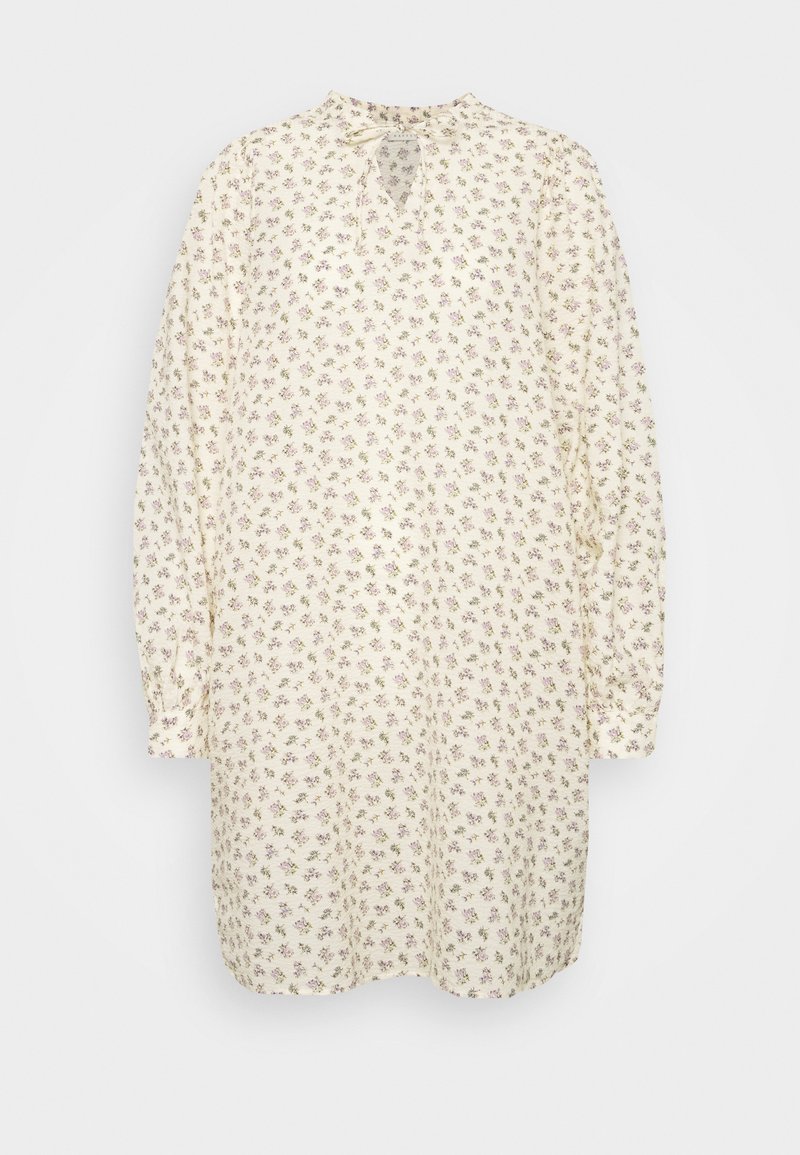 Vestido túnica floral em creme com pequenas flores roxas, mangas longas, gola alta e detalhe em buraco na frente. Textura de tecido suave.