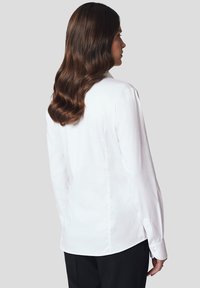 Biała koszula z długim rękawem i kołnierzykiem, charakteryzująca się gładką, miękką fakturą oraz dopasowanym krojem, prostym szwem z tyłu i mankietami na guziki.