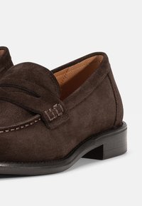 Brown suede loafers with a classic design, featuring a stitched upper and a slight heel, complemented by a smooth leather lining.