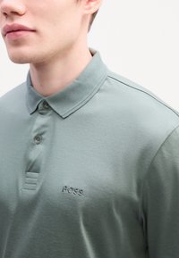 Dark green polo shirt made of smooth cotton. Features a button collar, three buttons at the neck, and "BOSS" logo embroidered in matching thread.