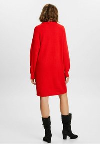 Czerwona, oversize dzianinowa sukienka z długimi rękawami i okrągłym dekoltem. W zestawie z czarnymi zamszowymi kozakami za kolano, tworzącymi kontrast.