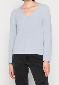 Pull en maille bleu clair avec un col en V et des manches longues, présentant un motif texturé à côtes. Associé à un jean foncé.