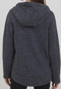 Giacca con cappuccio in tessuto grigio scuro melange, caratterizzata da un motivo testurizzato, design leggermente aderente e orlo curvo con tasche laterali.