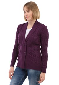 Lila gestrickte Strickjacke mit Kabelmustern, doppelten Knöpfen und einem Schalkragen. Mit gerippten Manschetten und Saum, kombiniert mit blauen Jeans.