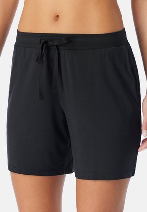 Close-up of a person wearing black drawstring shorts, showing the waist, navel, and upper thighs with one hand by their side.