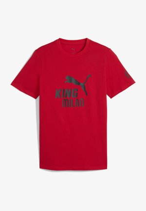 Raudonas medvilninis marškinėlis, išsiskiriantis pilku grafiniu piešiniu, vaizduojančiu šuoliuojantį pumą, ir tekstu "KING MILAN". Trumpomis rankovėmis ir klasikiniu apvaliu kaklu.