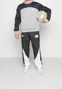Šedá a černá mikina s kapucí s bílými detaily, obsahuje přední kapsu; v kombinaci s černo-bílými tepláky, obě s logem Nike.