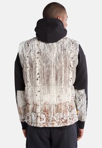 Pufferweste mit einem von der Natur inspirierten Druck, der Birkenbäume zeigt, schwarzen Kapuzenärmeln und einem strukturierten Stoff, der sich von einer glatten Oberfläche abhebt.