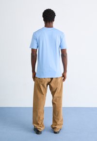 Light blue cotton t-shirt with short sleeves, paired with beige corduroy pants, seen from the back. Smooth texture and relaxed fit.
