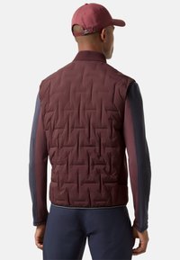 Weinrote gesteppte Weste mit hohem Kragen, marineblauen Ärmeln und figurbetonter Silhouette; kombiniert mit einer weinroten Mütze aus glattem Stoff.