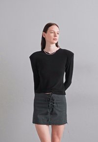 Μαύρη μπλούζα με μακριά μανίκια και στρογγυλή λαιμόκοψη, συνδυασμένη με μίνι φούστα σε γκρίζο χρώμα που διαθέτει λεπτομέρεια δέσιμο μπροστά. Απαλή ύφανση και εφαρμοστή σχεδίαση.