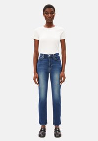 T-shirt blanc à manches courtes côtelé associé à un jean en denim bleu slim taille haute avec un léger délavage et un design à cinq poches.