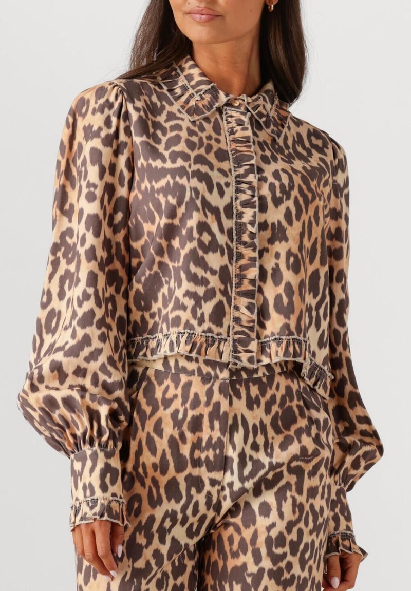 Vrouw in een bijpassende blouse en broek met luipaardprint, met gerimpelde afwerking op de blouseplacket, manchet en zoom.