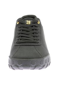 Zapatilla negra con parte superior texturizada, puntera redonda y cordones planos. Presenta una suela de goma con un patrón de panal y un logo en amarillo.