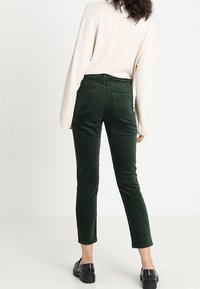 Gröna kordflöjlsbyxor med hög midja, slim fit och framfickor; kombinerat med en lösbeige tröja och svarta skor.