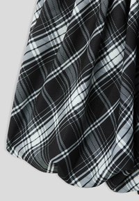 Tessuto a quadri bianco e nero con motivo a griglia diagonale, che mostra pieghe e texture su uno sfondo neutro.