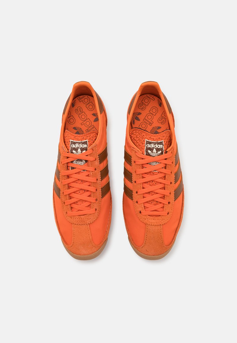 Zapatillas deportivas naranjas con rayas marrones, con parte superior de ante y sintético, plantilla texturizada y cordones redondos. Diseño clásico.