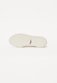 Suola di sneaker bianca con un motivo a spina di pesce, caratterizzata da un logo su una parte curva. Materiale in gomma morbida con leggero texture e grip.