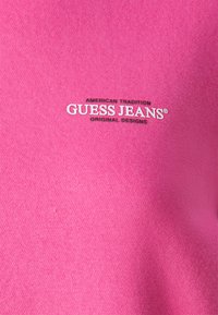 Roze katoenen sweatshirt met het "GUESS JEANS" logo in witte en zwarte tekst. De stof heeft een gladde textuur met een lichte stretch.