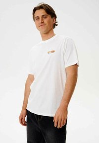 Hvid bomuld t-shirt med korte ærmer og rund halsudskæring. Har et lille orange logo på venstre bryst. Casual pasform, glat tekstur.
