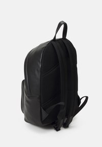 Svart ryggsekk med en glatt lærframside og teksturert mesh-bakside, med justerbare stropper og et bærehåndtak på toppen.