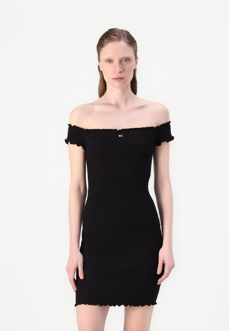 Robe noire à épaules dénudées en tissu texturé, design ajusté avec des bords volants et un subtil détail de logo à l'avant.