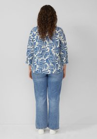 Blauw-witte blouse met een patroon en 3/4 mouwen, gecombineerd met lichtblauwe flared jeans en witte sneakers. Materiaal lijkt lichtgewicht.