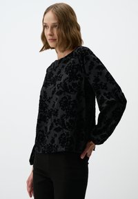 Zwart fluweel bloemen top met lange mouwen, ronde halslijn en textuur borduursel. Gepaard met strakke zwarte broeken, minimalistisch ontwerp.