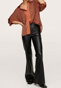 Camicia oversize a strisce color ruggine con colletto, abbinata a pantaloni a campana in pelle nera a vita alta. Tessuto liscio e vestibilità su misura.