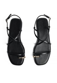 Mustad mustad sandaalid, millel on mitu ristatud rihma, lame talla ja kuldne aktsent varba lähedal. Siledat tekstuuri ja minimalistlikku disaini.