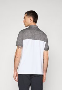 Polo skjorte med en heather grå overdel og solid hvit underdel. Har en krage, korte ermer, og synlige tatoveringer på modellens arm.