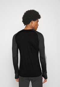 Svart långärmad träningsblus med grå detaljer. Har en figurnära passform och en smidig textur, utformad för komfort under fysisk aktivitet.