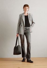 Šedý pruhovaný blazer, černý top, tmavé džíny s roztrhanými lemy a černé kotníkové boty. Nese černou tašku s dlouhým popruhem.