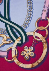 Stampa di tessuto colorato con catene dorate, una tracolla rosa e un nastro a righe verdi. Include un charm a forma di fiore in oro con strass.