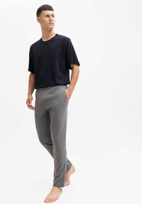 Maglietta nera a maniche corte, pantaloni grigi leggeri con elastico in vita, texture liscia, vestibilità comoda, piedi nudi. Outfit semplice e informale.