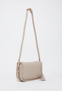 Sac bandoulière en cuir beige avec une finition texturée, quincaillerie dorée et un accent de frange. Bandoulière ajustable pour un port polyvalent.