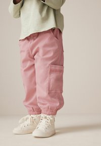 Pantaloni cargo roz cu manșete elastice, având buzunare laterale. Asortați cu teniși albi cu glezna înaltă. Top verde deschis cu mânecă lungă deasupra.