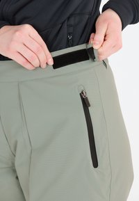 Vaaleanvihreät housut, joissa on vetoketjullinen tasku, säädettävä vyötärö tarranauhalla ja teksturoitu kangas. Sopivat ulkoiluun.