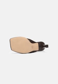 Chaussure à talon marron foncé avec semelle en cuir, bout carré et talon rectangulaire étroit vue du côté de la semelle.