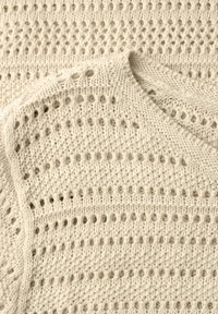 Tissu tricoté de couleur crème avec un motif ajouré comprenant des rangées de petits trous et des points texturés.