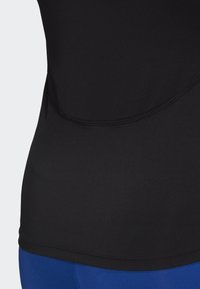 Top deportivo negro ajustado fabricado con tela suave, con un diseño de costura curva y un dobladillo extendido para mayor cobertura.